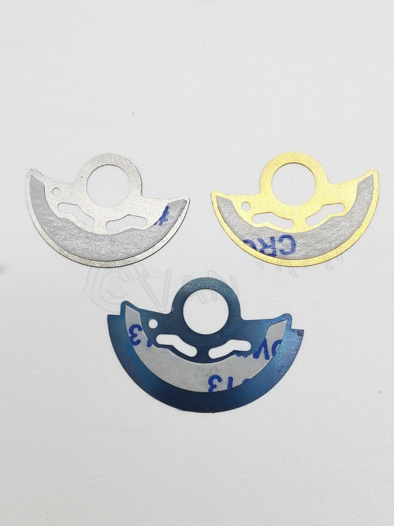 May include: Three metal engine parts in different colors: silver, gold, and blue. Each part has a circular hole in the center and a curved shape.