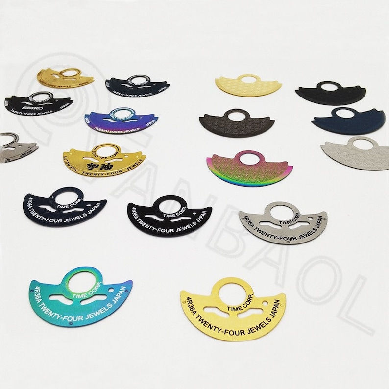 May include: Assortment of 10 different colored metal watch movement parts. Each part is a crescent shape with a hole in the center. The parts are labeled with the text "TIME CORP" and "TWENTY-FOUR JEWELS JAPAN".