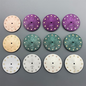 May include: A collection of twelve watch dials in various colors, including gold, purple, green, and silver. Each dial features a radial pattern, gem-like hour markers, and the word "AUTOMATIC".