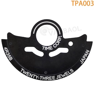 May include: Black metal watch movement part with white text that reads "TIME CORP. TWENTY-THREE JEWELS JAPAN 4R35B".
