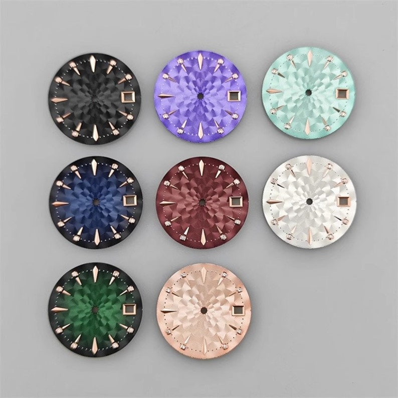 K&ouml;nnte beinhalten: Neun verschiedene farbige Zifferbl&auml;tter mit einem Diamantenmuster. Die Zifferbl&auml;tter sind alle gleich gro&szlig; und gleich geformt und alle aus Metall. Die Farben der Zifferbl&auml;tter sind Schwarz, Lila, Hellblau, Blau, Rot, Silber, Gr&uuml;n und Rosa.