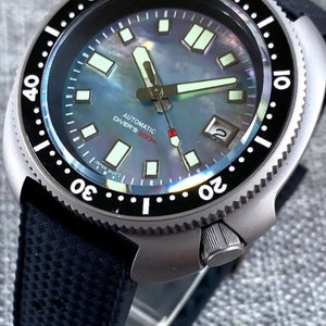 Może przedstawiać: Czarny i srebrny zegarek na rękę z czarnym paskiem z gumy. Tarcza zegarka jest biała z czarnymi oznaczeniami i tekstem "Automatic Diver's 200m".