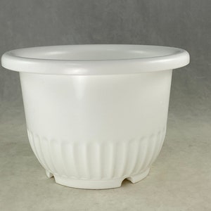 May include: A white plastic planter with a fluted design around the bottom. The planter is round and has a wide rim.