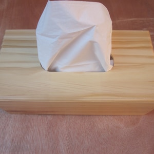 May include: A wooden tissue box holder with a natural wood finish. The box has a rectangular opening for tissues.