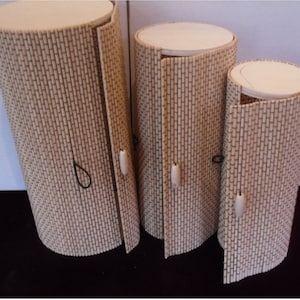 May include: Three cylindrical boxes made of woven bamboo with lids that open like doors. The boxes are different sizes and have wooden knobs.