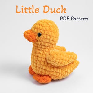 May include: A crocheted yellow duck with orange feet and a black eye. The duck is sitting on a white surface. The text "Little Duck PDF Pattern" is above the duck.