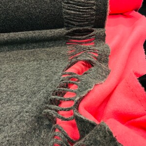 Puede incluir: Primer plano de una tela gris con un borde de flecos. La tela está doblada sobre una tela de color rosa brillante.