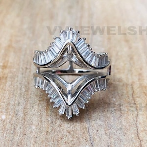 May include: A silver ring with a unique design featuring two rows of baguette-shaped stones that form a V shape. The ring is set on a wooden surface.