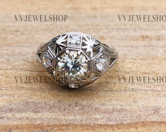 May include: A silver ring with a large, clear, octagonal-shaped center stone surrounded by smaller, clear stones. The ring has a delicate, intricate design with a floral motif.