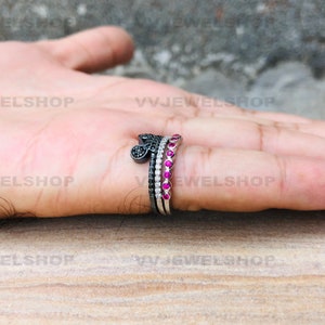 May include: A set of three rings. One ring features a black Mickey Mouse head design, another has a row of white stones, and the third has a row of red stones. The rings are silver in color.