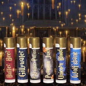 May include: Six different flavored lip balms in gold tubes with labels featuring Harry Potter themed designs. The labels include "Butter Beer", "Gilly Water", "Polyjuice Potion", "Pumpkin Juice", "Unicorn Blood", and "Wolfsbane".