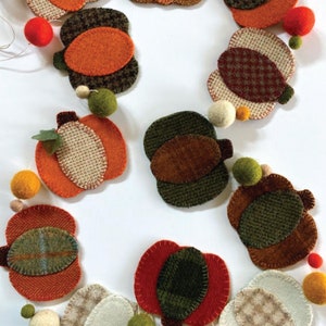 May include: A felt garland featuring a pumpkin theme. The garland is made from felt pumpkins in a variety of colours and patterns, including orange, green, brown, and beige. The pumpkins are stitched together with white thread. The garland is adorned with small felt balls in various colours, including red, white, and green. The garland is ideal for autumn decorating.