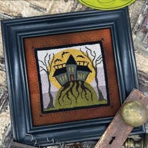May include: Framed punchneedle embroidery titled "Haunted Manor." The artwork features a spooky house on a hill with a yellow moon and bare trees. The frame is dark blue, and the artwork is 5" x 5". The brand name "Threads that Bind" is also visible.