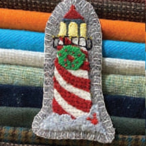 May include: A felt Christmas ornament shaped like a lighthouse with red and white stripes, a green wreath with a red bow, and a white snowy base.