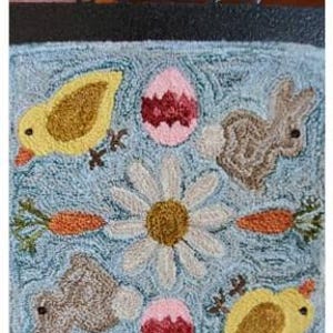 May include: A blue and white needlepoint design featuring a daisy, two yellow chicks, two brown bunnies, and two pink eggs. The design is titled "Garden Gals April".