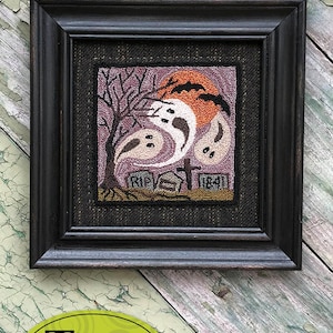 May include: A framed punch needle embroidery design featuring three ghosts, a tree, and a full moon with bats flying overhead. The embroidery is on a purple background with brown and black accents. The frame is black and the text "RIP" and "1841" are visible on the embroidery. The title "711 - Spooktacular Night" and the size "5 1/2" x 5 1/2" Punchneedle Embroidery" are printed below the image.