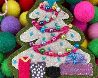 May include: A handmade Christmas tree ornament with a green outline, decorated with a star, colorful beads, and small gift boxes. The ornament is surrounded by colorful felt balls in shades of red, pink, yellow, green, and purple.