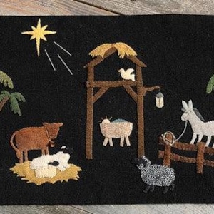 May include: A rectangular fabric wall hanging featuring a black center panel with a nativity scene applique including a yellow star, brown stable, palm trees, a cow, a sheep, a donkey, and a manger. The side panels are tan with printed text.