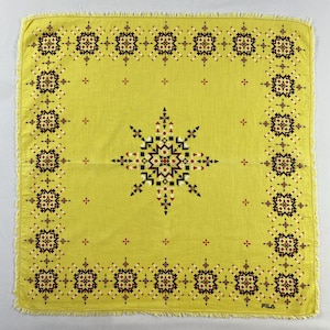 May include: A square, yellow handkerchief with a geometric pattern. The design features a central starburst and a border of repeating floral motifs in black, white, and red. The edges are fringed, and the word "FILA" is printed in the bottom right corner.