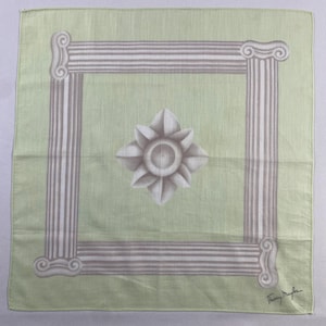 May include: A green silk scarf with a white and gray floral design and a white border. The scarf has a white frame with a repeating pattern of columns. The scarf is signed "Thierry Mugler" in the bottom right corner.