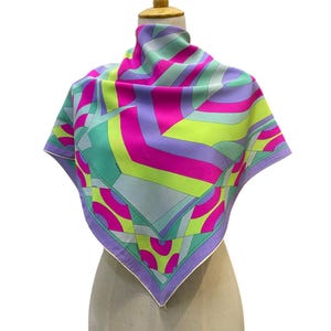 Pode incluir: Um lenço quadrado de seda com um padrão geométrico arrojado em tons vibrantes de rosa choque, verde lima, lavanda e azul claro. O design consiste em linhas angulares e formas curvas que se cruzam, com uma bainha branca bem definida.