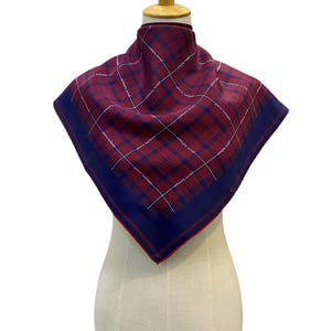 May include: A square scarf with a red and navy blue plaid pattern. The scarf has a navy blue border and white text that reads "pierre balmain". The scarf is displayed on a mannequin.