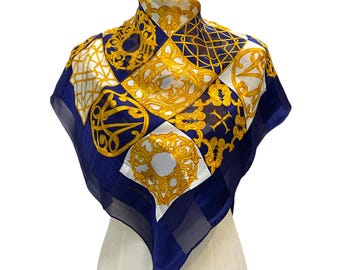 May include: A blue and white silk scarf with a gold patterned design. The scarf features a geometric pattern with ornate details. The brand name "LANVIN" is visible in the lower right corner.