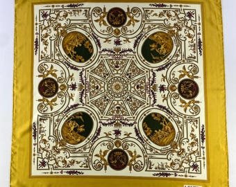 May include: A gold and white silk scarf with a repeating pattern of ornate designs and figures. The scarf has a gold border and the word "LANCEL" is printed in the bottom right corner.