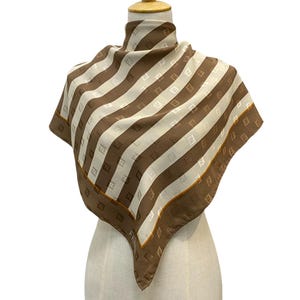 May include: A brown and white striped silk scarf with a repeating pattern of the letter "F" in a smaller size. The scarf is displayed on a white mannequin.