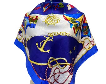 May include: A blue and white silk scarf with a nautical theme. The scarf features anchors, ropes, and stars. The brand name "Lancel" is visible in the bottom corner.