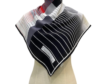 May include: A square silk scarf featuring a geometric pattern of black, white, gray, and red stripes. The design includes a prominent black section with white pinstripes and the text Christian Dior printed in a white rectangular border.