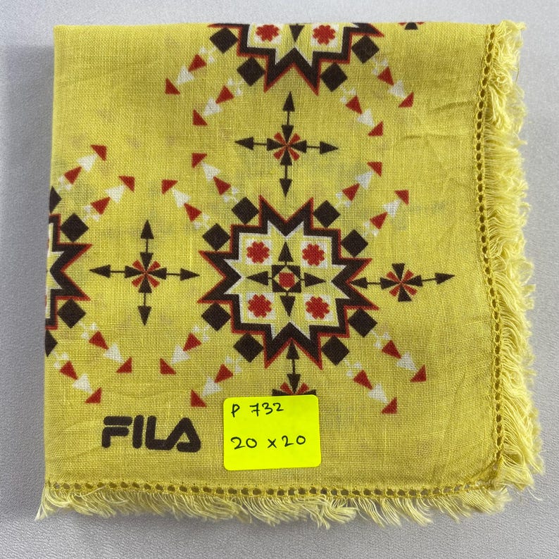 May include: Yellow FILA handkerchief with a geometric pattern in red, brown, and white. The handkerchief has a fringed edge and the FILA logo in black. A yellow sticker indicates the size is 20 x 20 inches.