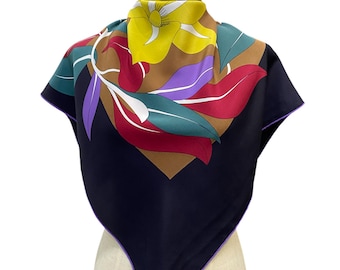 May include: A black silk scarf with a colorful floral design. The scarf features a yellow flower with red, purple, and green leaves. The scarf is trimmed with a purple border and has the word "CARES" printed on the bottom corner.