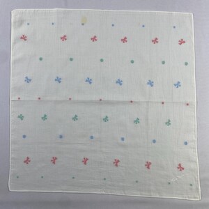 May include: A white cotton handkerchief with a repeating pattern of blue, green, and pink bows. The handkerchief has a subtle, faded appearance.