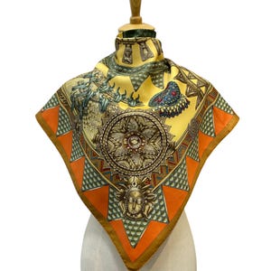 May include: A square silk scarf featuring a vibrant yellow background with orange triangular borders and green patterned accents. The design includes a central circular medallion, a stylised face mask, and various intricate ornamental motifs.