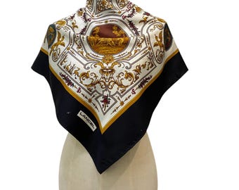 May include: A square silk scarf featuring a white center with intricate gold and burgundy baroque-style patterns, a central circular illustration, and a wide black border. The word LANCEL is printed in white on the black border.