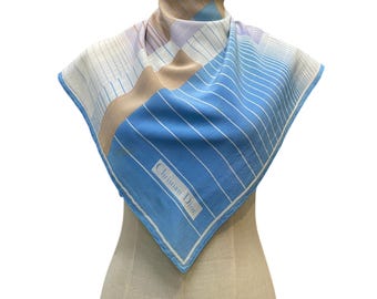 Könnte beinhalten: Ein quadratisches Tuch mit einem geometrischen Muster aus blauen, beigefarbenen und weißen Streifen. Das Design enthält einen markanten blauen Bereich mit feinen weißen Linien und dem Schriftzug Christian Dior in einem weißen Rahmen unten.