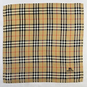 May include: Tan, black, white, and red plaid handkerchief with the Burberrys logo in the bottom right corner. The handkerchief has a classic check pattern, with a tan background and intersecting lines.