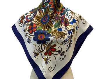 May include: A white silk scarf with a navy blue border and a floral pattern in shades of red, blue, yellow, and green. The scarf features the text "LANCEL" in the lower right corner.