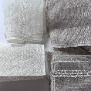 Op de afbeelding: Vier stukken geweven stof in twee verschillende kleuren. Twee stukken zijn lichtbeige en twee stukken zijn donkerbeige. De stof heeft een losse weving en is licht transparant.