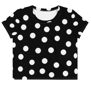 May include: Black crop top featuring a white polka dot design. The top has short sleeves and a round neck. The white spots are uniformly distributed across the material.