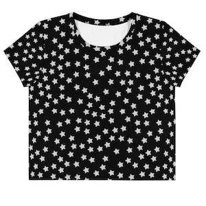 May include: Black crop top featuring a white star pattern. The shirt has a scoop neck and short sleeves. The star pattern is evenly distributed across the fabric. This top is suitable for casual wear and is a versatile addition to any wardrobe.