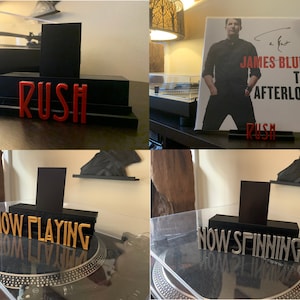 May include: A black vinyl record display stand with a red "RUSH" sign. The stand holds a record album. The album cover features James Blunt and the album title "The Afterlove". Other stands say "NOW PLAYING" and "NOW SPINNING".