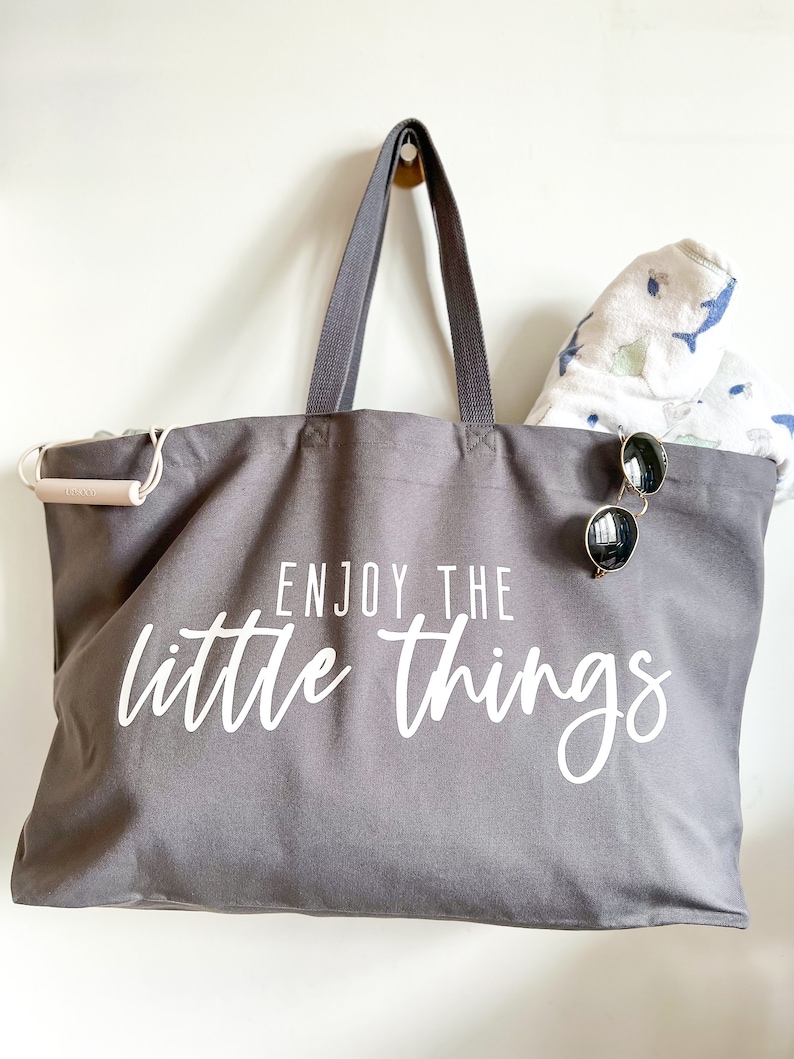 Perfect beach bag, travel companion and mothers best friend. Oversized tote in a thick durable grey canvas which says “Enjoy the little things”. These totes come in 4 different text options, two text colors and 4 tote color options.