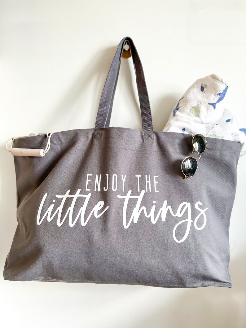 Perfect beach bag, travel companion and mothers best friend. Oversized tote in a thick durable grey canvas which says “Enjoy the little things”. These totes come in 4 different text options, two text colors and 4 tote color options.
