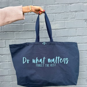 Pode incluir: Uma bolsa tote azul escura com o texto "Do what matters, forget the rest" em azul claro. A bolsa tem al&ccedil;as pretas e um pequeno logotipo "MTE".