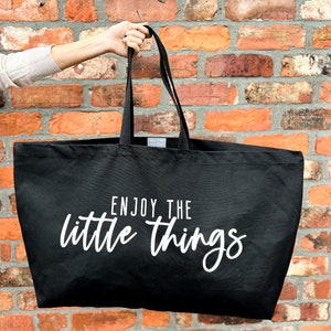 Oversized tote in a thick durable black canvas which says “Enjoy the little things”. These totes come in 4 different text options, two text colors and 4 tote color options.