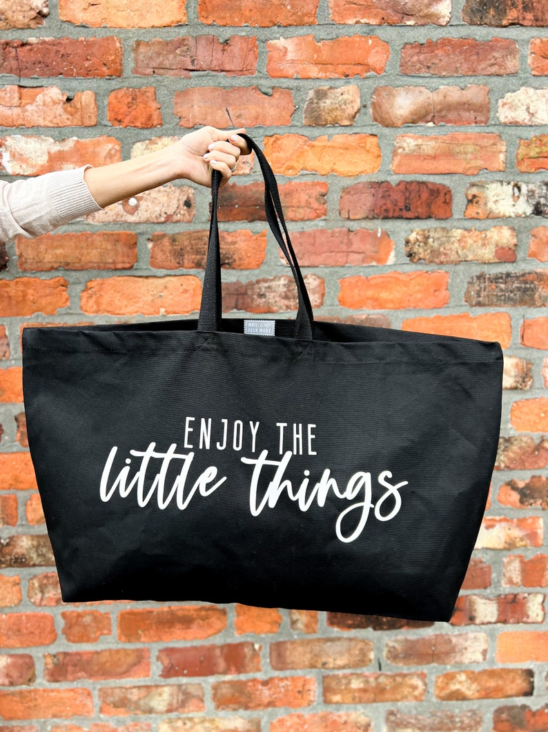 Oversized tote in a thick durable black canvas which says “Enjoy the little things”. These totes come in 4 different text options, two text colors and 4 tote color options.