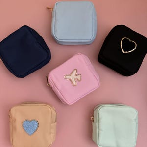 Puede incluir: Seis pequeñas bolsas con cremallera de varios colores con diferentes diseños bordados. Las bolsas son azul claro, azul marino, rosa, beige, verde menta y negro. Los diseños incluyen un corazón, un avión y un corazón con una textura esponjosa.