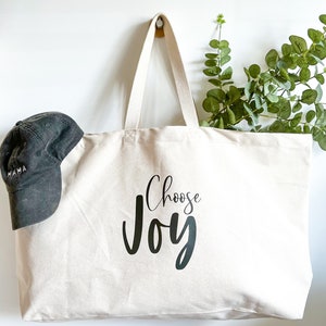 Oversized tote in a thick durable natural canvas which says “Choose Joy”. These totes come in 4 different text options, two text colors and 4 tote color options.